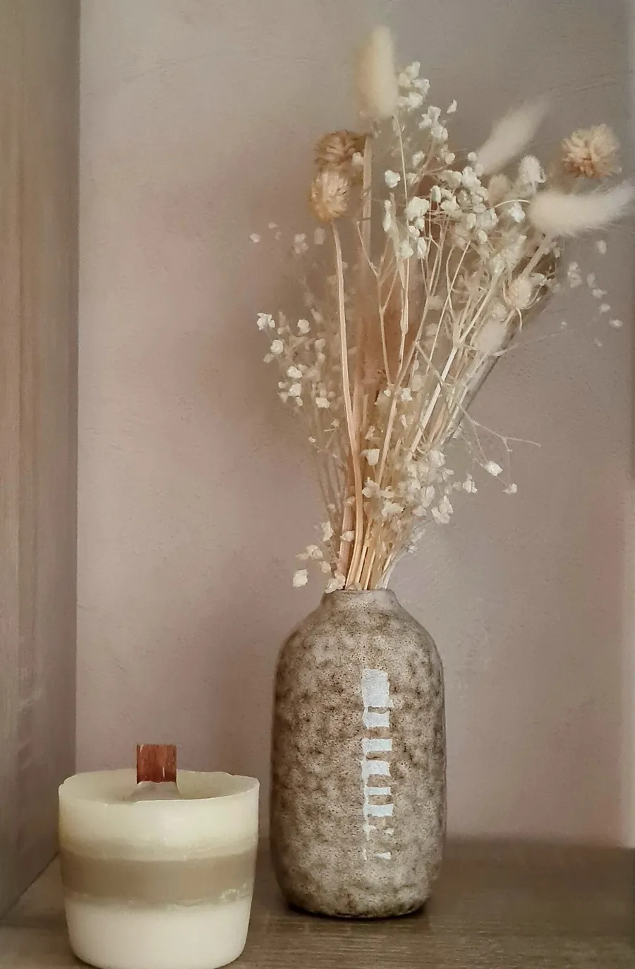 Un vase de fleurs séchées et une bougie, sur une étagère du cabinet